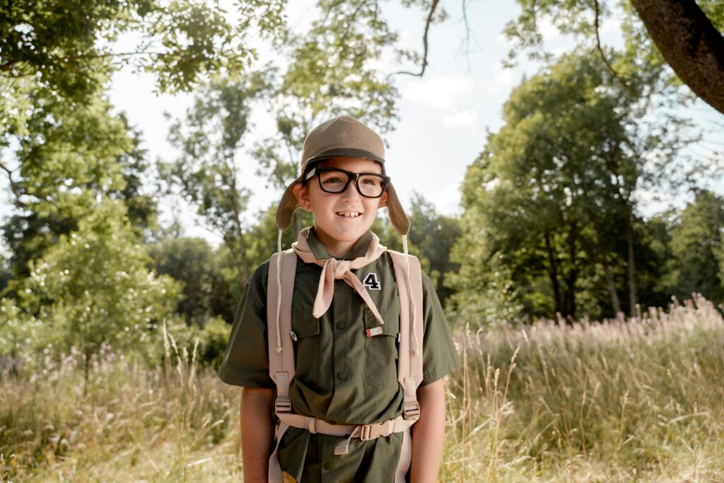 Young boy scout in uniform smiling in an outdoor setting, enjoying nature.